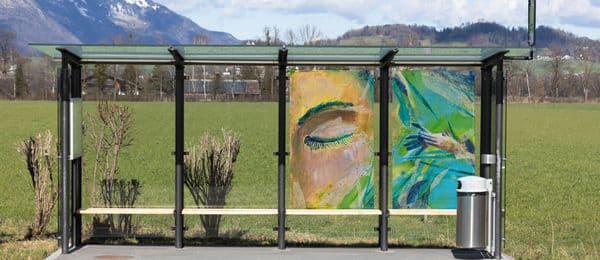 Das Bild zeigt ein Bushaltestelle mit einem gläsernen Wartehäuschen und einem Bildkunstwerk, gemalt auf das Glas der Rückwand.